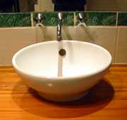 A vitreous china vessel inset into a timber top, with wall mounted taps and spout.